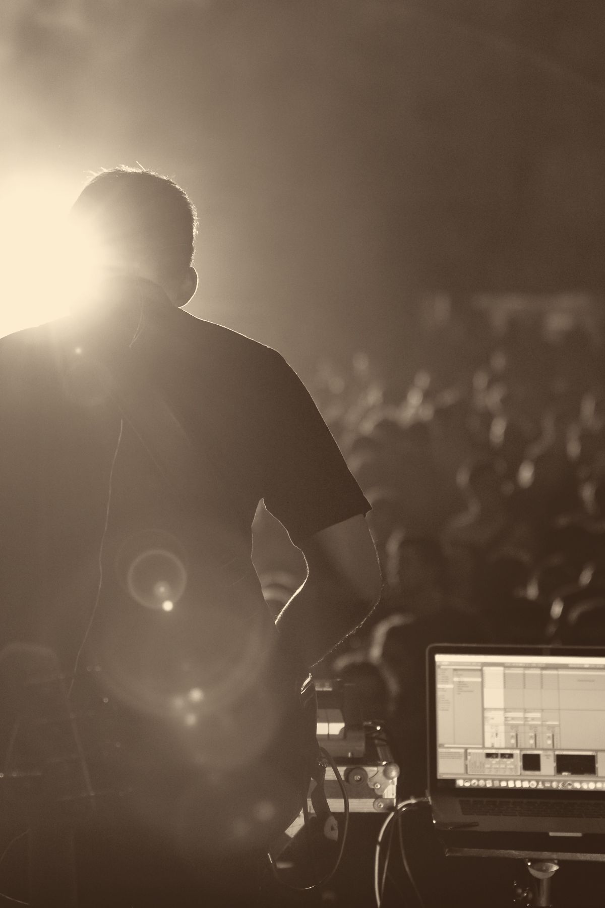 A producer silhouetted against stage light, performing for a small live audience